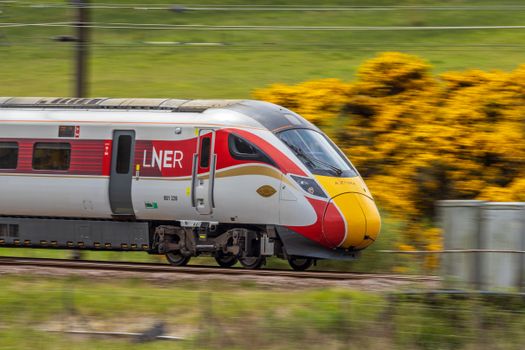 High-speed LNER train traveling through scenic countryside with yellow flowers.