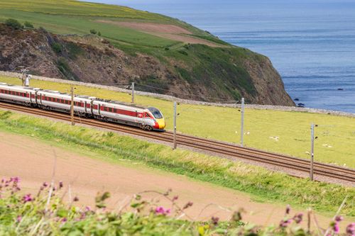 Free Passenger train travels along a scenic coastal route with stunning views and greenery. Stock Photo