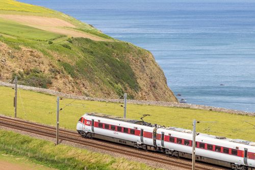 Free LNER train travels along picturesque coastline near cliffs and ocean under a clear sky. Stock Photo