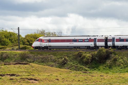 Free LNER Azuma train travels through scenic countryside landscape on a cloudy day. Stock Photo