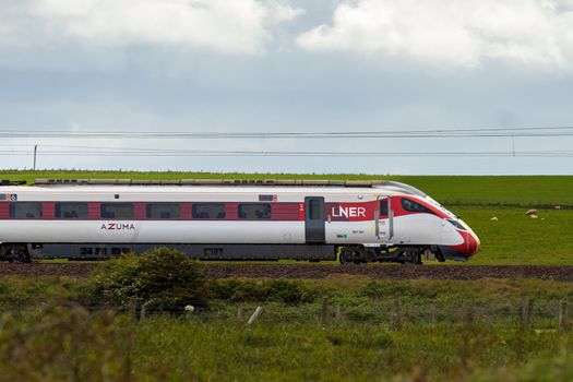 LNER Azuma train traveling through lush green countryside under cloudy skies.