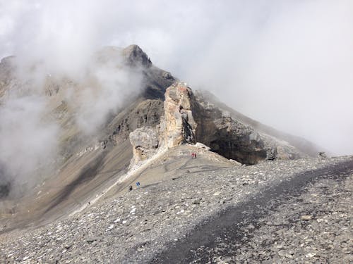 Breathtaking scenery of high rocky mountain peak hidden under gray clouds in wild valley