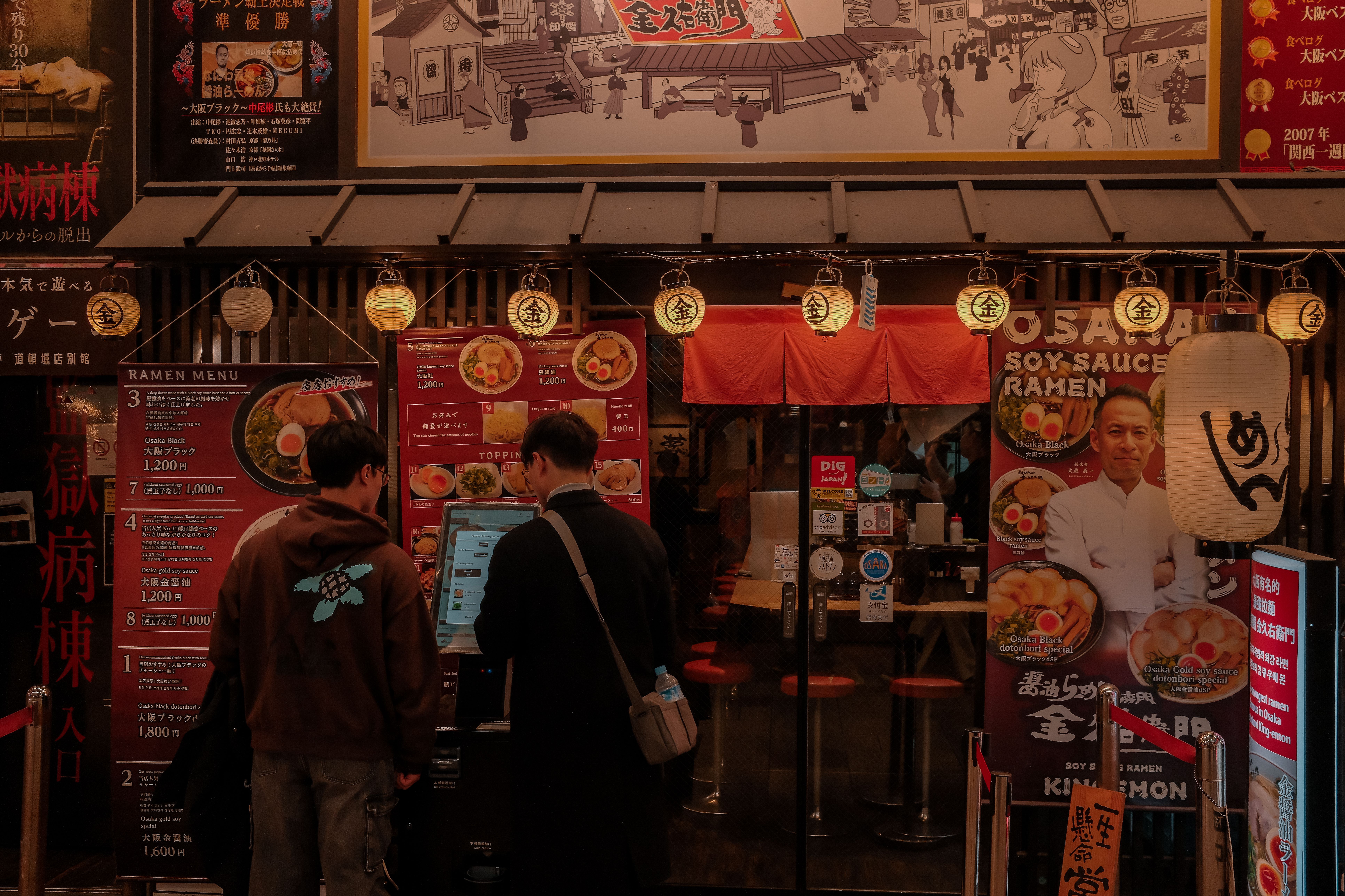 Customers ordering at a traditional Japanese ramen restaurant with colorful signage and lanterns.