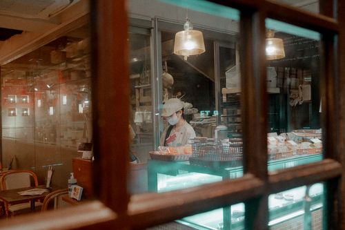Free Warm-lit bakery captured from outside, showcasing a staff member working inside the cozy cafe. Stock Photo