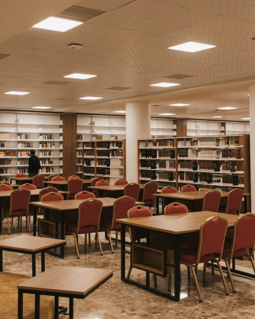 Free A spacious modern library featuring red chairs and wooden tables against filled bookshelves. Stock Photo