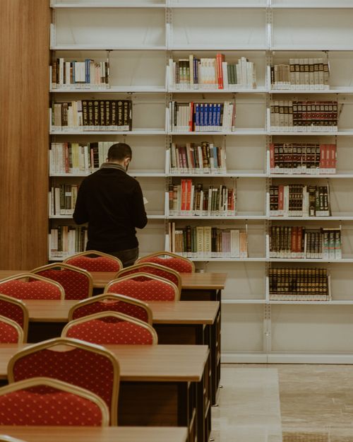 Free A man browsing books in a library with red chairs and rows of bookshelves. Stock Photo