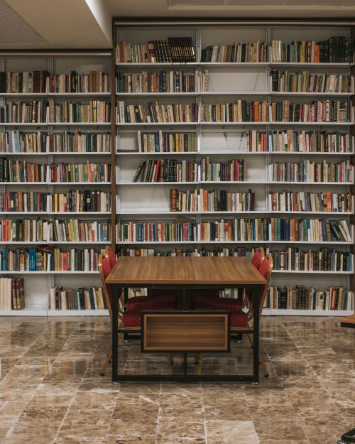 Free Quiet library scene with wooden table and extensive bookshelves filled with books. Stock Photo