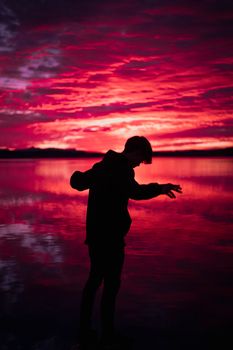 A captivating silhouette of a man against a vivid red and pink sunset sky reflecting on water.