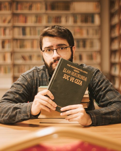 Free A man holding a book in a library with shelves in the background, captured at day. Stock Photo