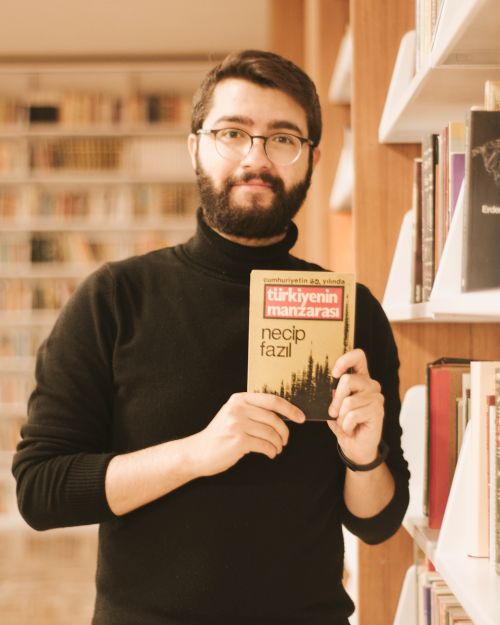 Free Man in library holding a book, surrounded by shelves of books, creating a warm, scholarly atmosphere. Stock Photo