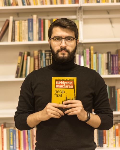 Free A man with glasses holds a book in a library setting, standing before bookshelves. Stock Photo
