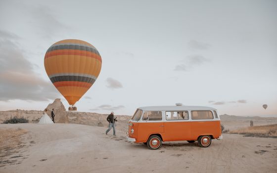 Couple celebrating wedding in front of hot air balloon with vintage van in scenic landscape.