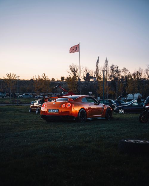 Free Stunning orange sports car parked outdoors during sunset in Ankara, Türkiye with a flag backdrop. Stock Photo