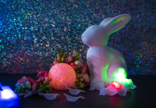 Free White bunny figurine surrounded by glowing lights and flowers, against a glittery backdrop. Stock Photo