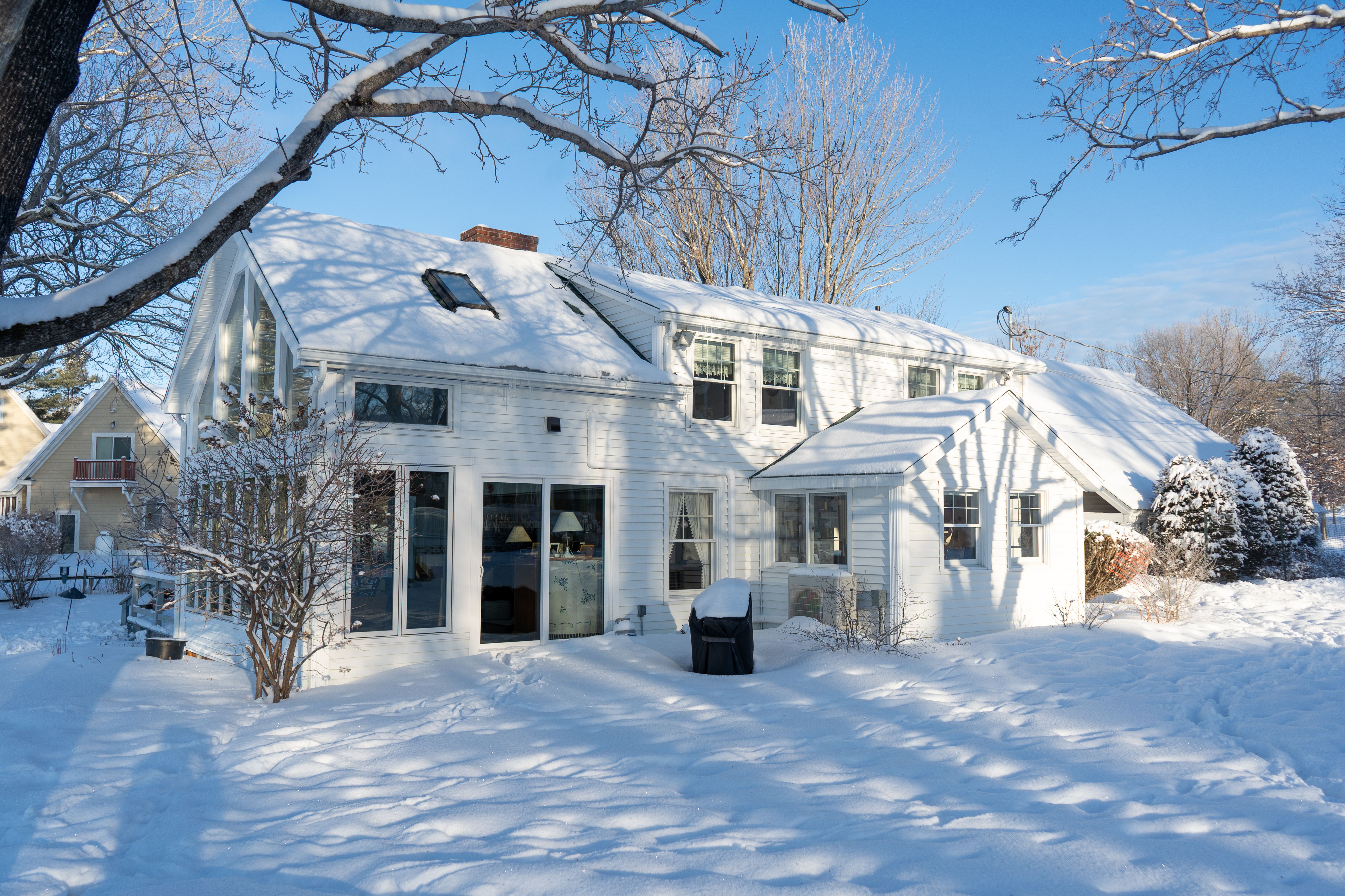 A picturesque white house blanketed in snow under a blue sky, showcasing winter's beauty.