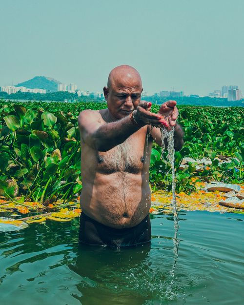 Free Senior man in sacred ritual at a lush Mumbai lake with urban skyline backdrop. Stock Photo