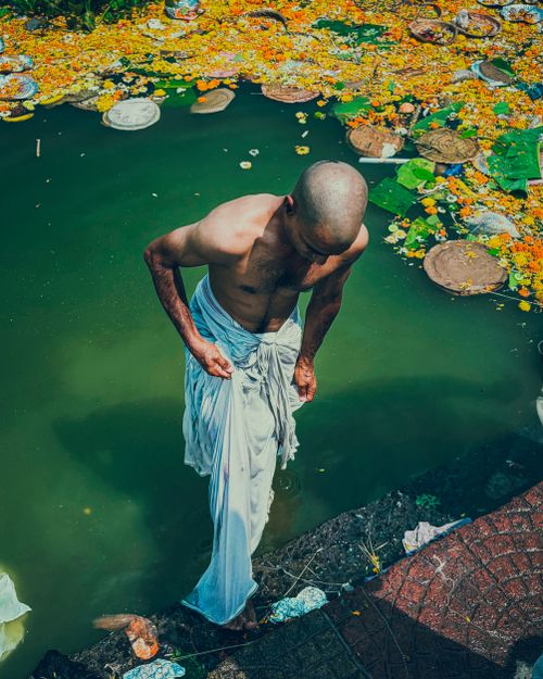 Free Man stepping out of a ritual bathing pool surrounded by flowers in Mumbai, India. Stock Photo