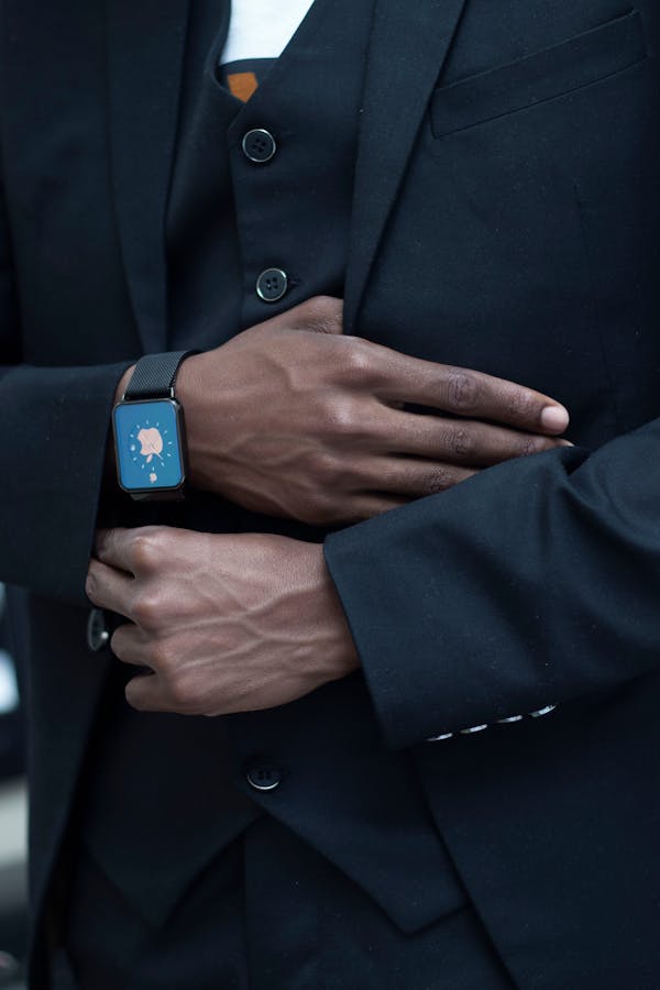 Anonymous person adjusting suit of unrecognizable African American gentleman in elegant outfit with modern smart watch