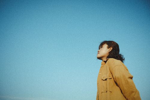 Free From below side view of young ethnic wistful female in jacket contemplating blue cloudless sky in daylight and looking away Stock Photo