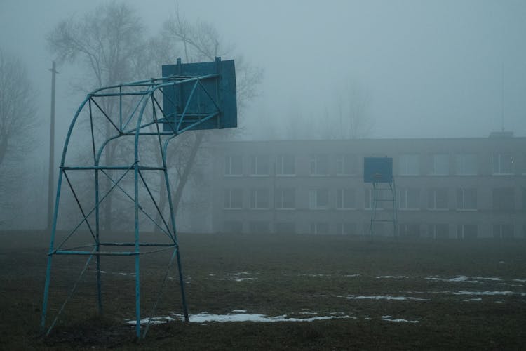 School Building Behind Basketball Field With Backboards In Windy Weather