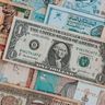 A one US dollar bill resting on top of a colorful assortment of international banknotes from various emerging markets.