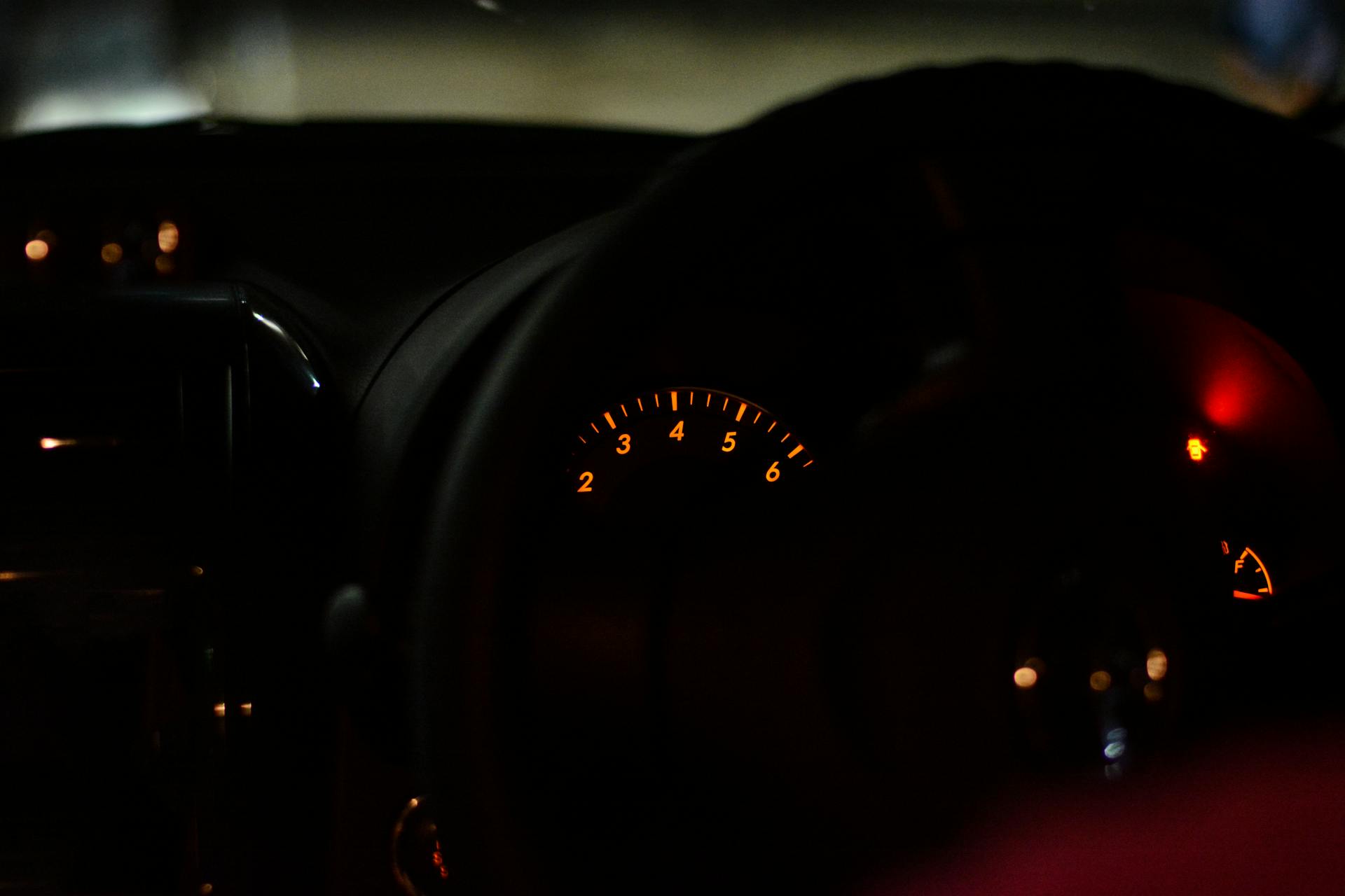 Close-up view of a car dashboard at night, showcasing illuminated gauges and indicators.