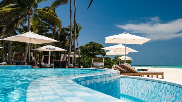 Luxurious resort poolside with umbrellas and palm trees on a sunny day by the ocean.