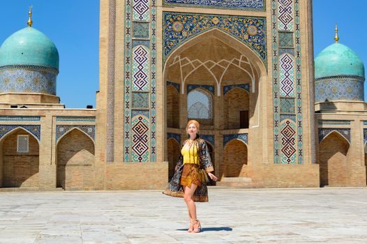 Woman in vibrant attire in front of a majestic Uzbek mosque with turquoise domes.