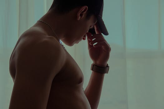 A shirtless man in contemplation, silhouetted against indoor curtains.