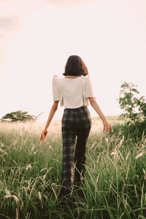 Mujer En Top Blanco Y Pantalones A Cuadros Caminando Sobre La Hierba Verde