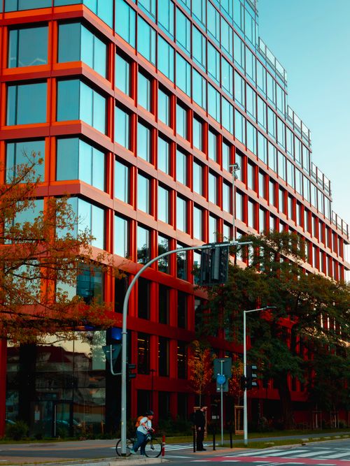 Free Striking red building facade in Wrocław, Poland captured at sunset with cyclists passing by. Stock Photo