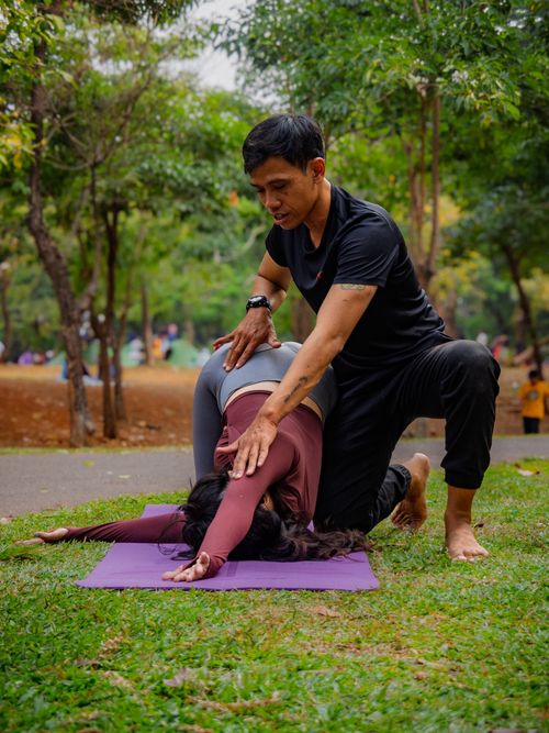 Free Yoga instructor assisting student with pose in Jakarta park. Stock Photo