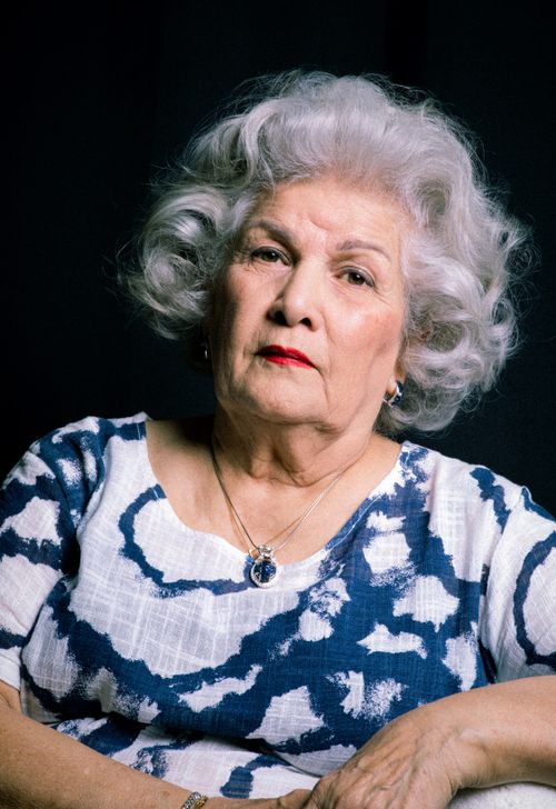 Free Elegant elderly woman with curly grey hair in a stylish outfit sitting indoors. Stock Photo