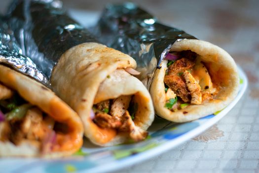 Tantalizing chicken shawarma wraps with fresh vegetables and sauce, wrapped in foil, on a plate.