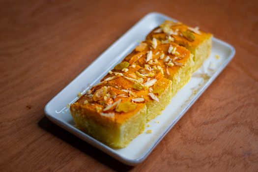 Close-up of a traditional Indian sooji cake garnished with almonds and raisins on a white plate.