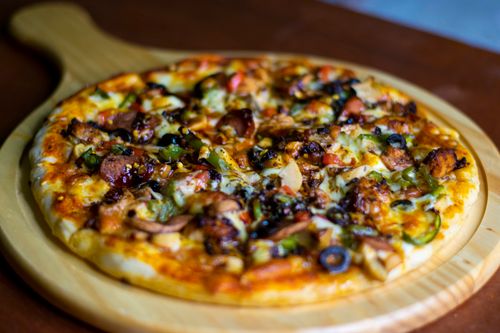 Free Close-up of a richly topped homemade pizza on a wooden board, perfect for food lovers. Stock Photo