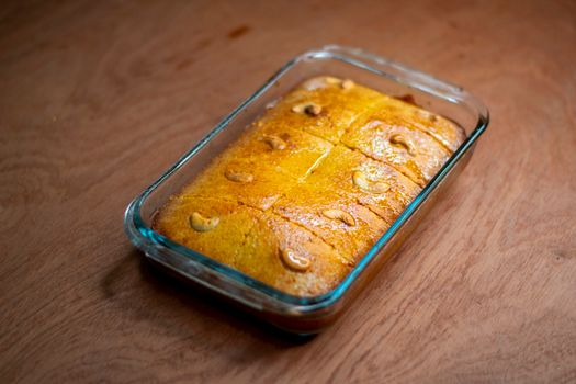 Freshly baked cashew cake in a glass dish on a wooden table, perfect for dessert lovers.