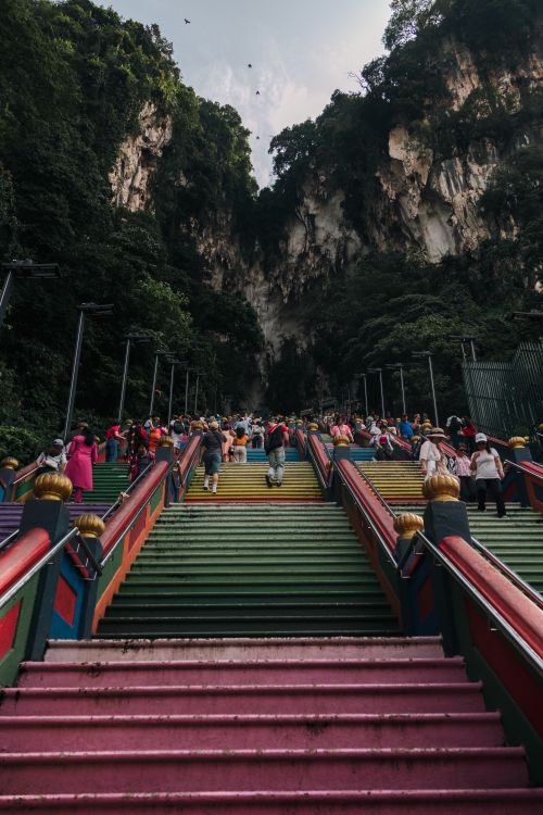 Free Visitors climb vibrant steps leading to Batu Caves, Selangor under lush forest cliffs. Stock Photo