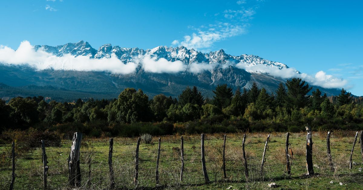 Snow-capped mountains and rustic fence under a clear blue sky.