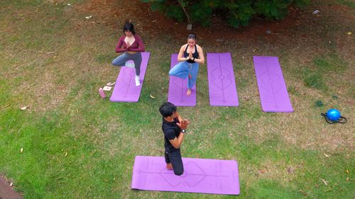 Free Aerial view of people practicing yoga on mats in a lush Jakarta park. Stock Photo