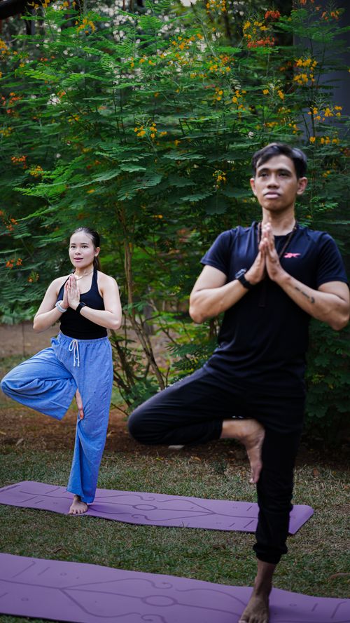 Free Two adults practicing yoga outdoors in a lush Jakarta park, focusing on balance and tranquility. Stock Photo