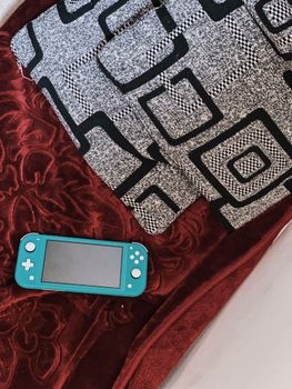 Top view of modern video game controller representing input device with display and buttons on velvet plaid near fabric with square ornament in bedroom in apartment