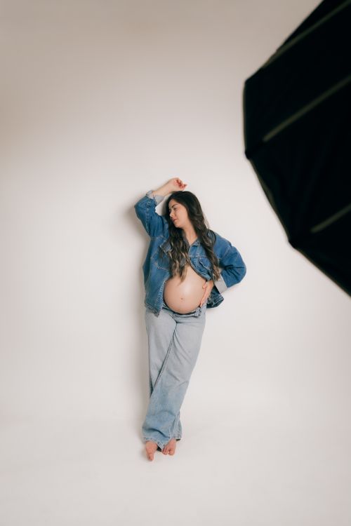 Free Elegant maternity portrait featuring a woman in denim against a minimalist background. Stock Photo