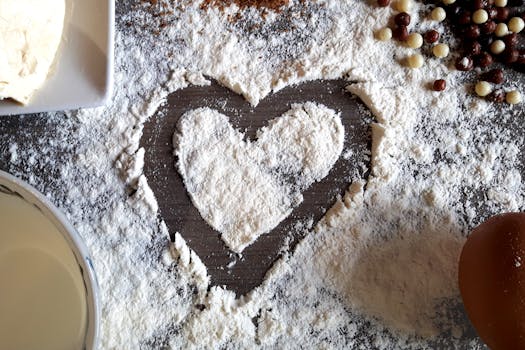 Close-up of a heart shape created in flour, surrounded by baking ingredients.