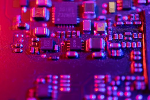 Macro shot of an electronic circuit board with vivid purple and pink lighting, highlighting components.