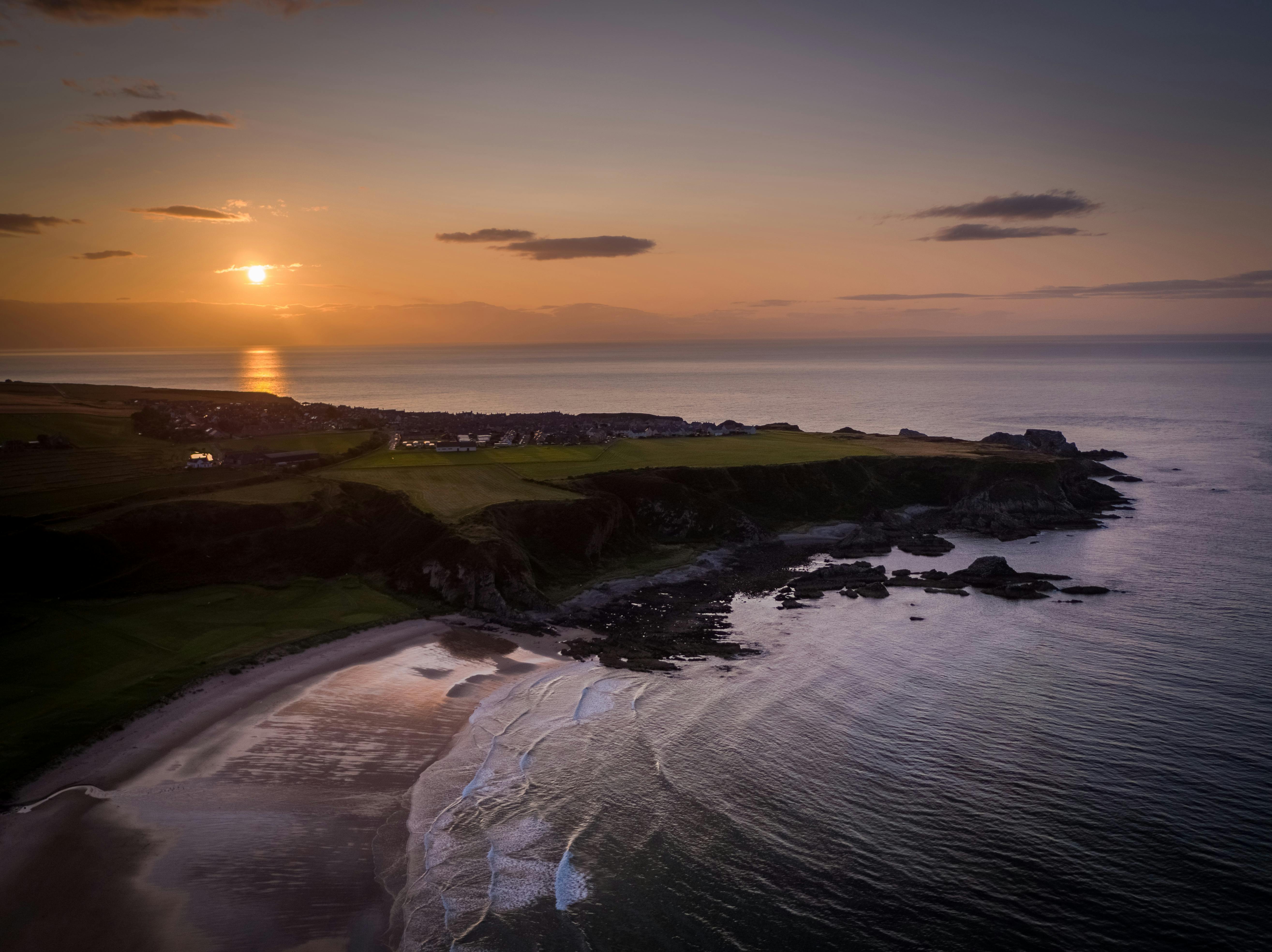 Aerial view of Cullen Bay, Scotland at sunset showcasing stunning coastal cliffs and serene sea waves.