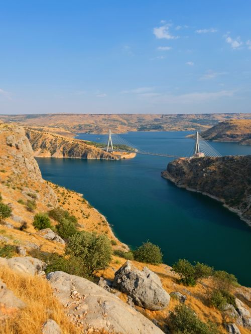 Free Beautiful landscape of a bridge spanning a tranquil river gorge, surrounded by rocky cliffs and blue sky. Stock Photo