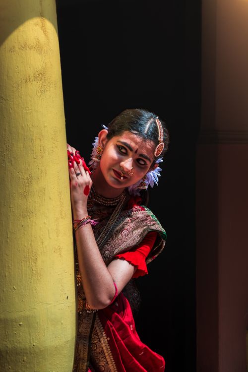Free Elegant Indian woman in traditional saree with floral accents peeking from behind a pillar. Stock Photo