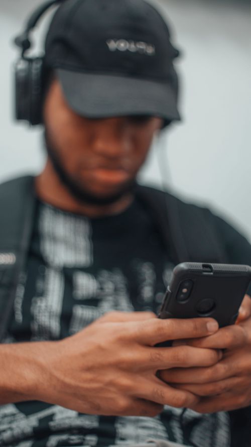 Free A young man wearing headphones focuses intently on his smartphone while outdoors. Stock Photo
