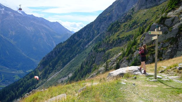 Hiker photographing breathtaking mountain landscape with cable car view.